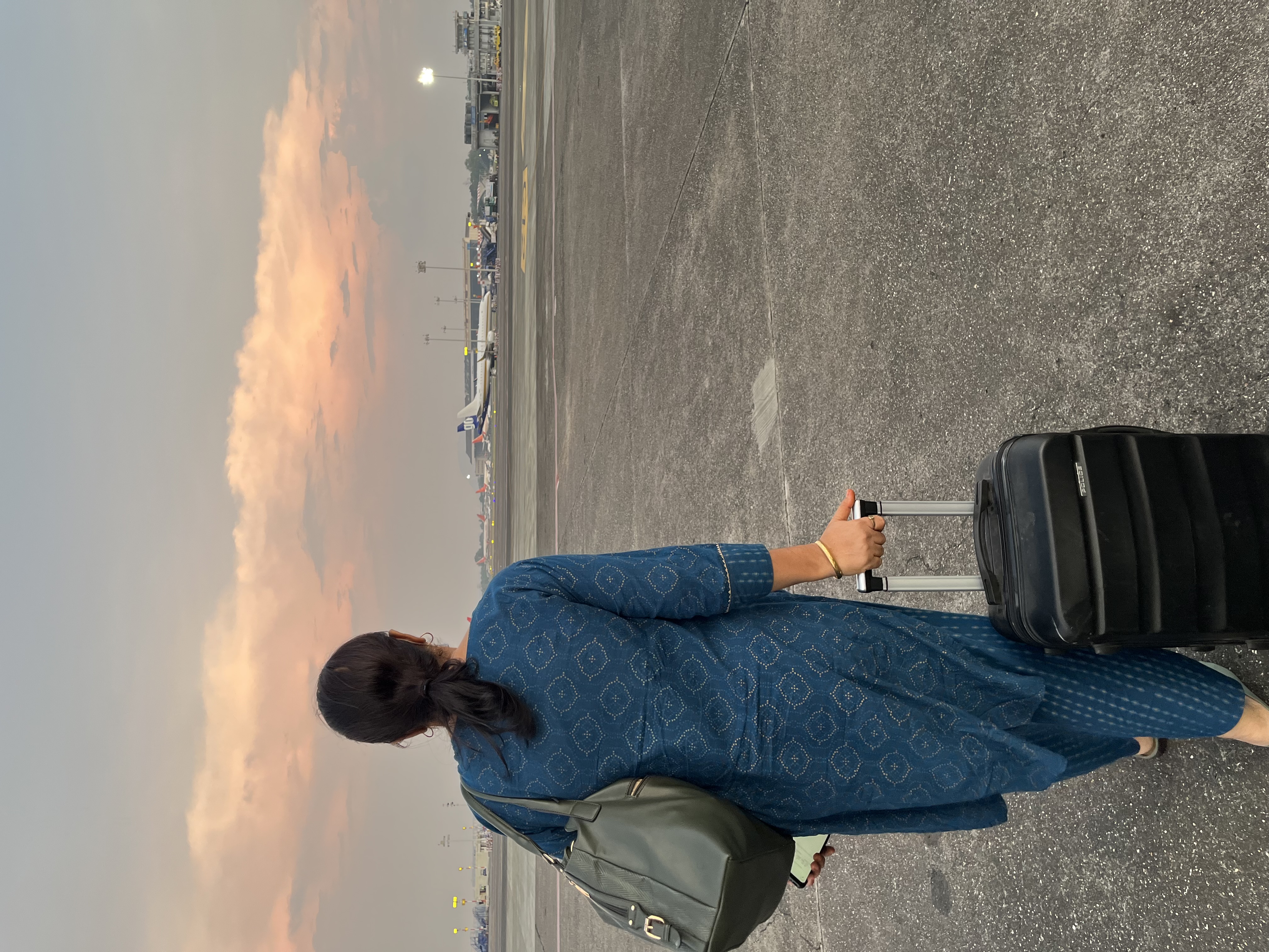 A picture of Tushar's mother on the airport runway with a suitcase in hand and a purse on shoulder